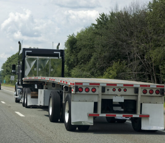 Commercial flat bed truck traveling through road.