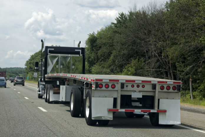 dreamstime_xxl_79874202 Commercial flat bed truck traveling through road.